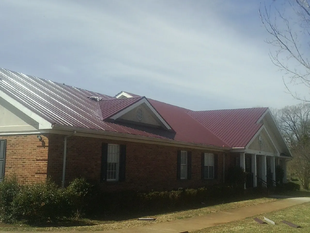 Red metal roof with gabled entries on a long brick building, from a Hail Damage Roof Repair job in Wooster