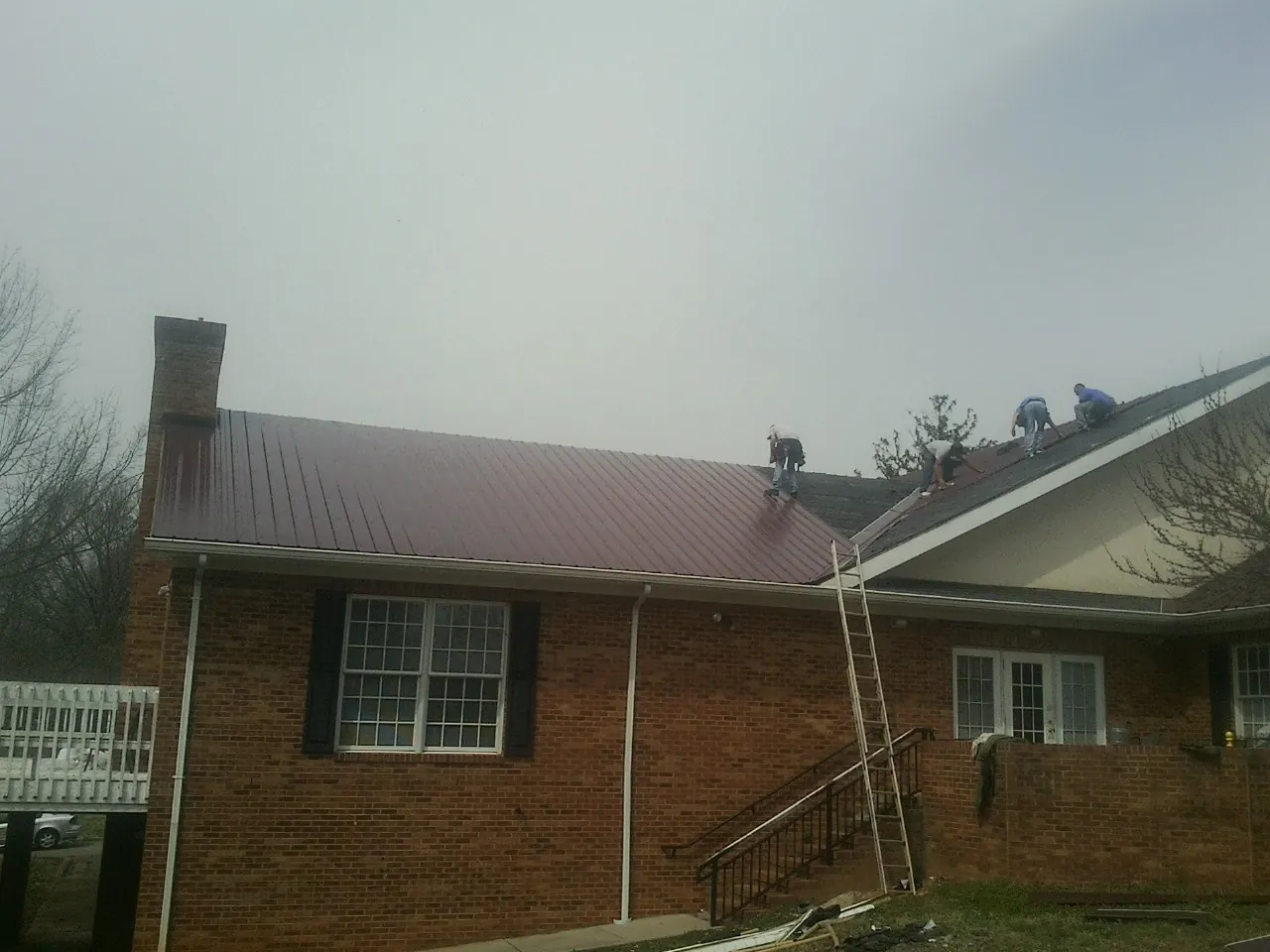 Crew setting red metal roofing panels on a brick home in Wooster