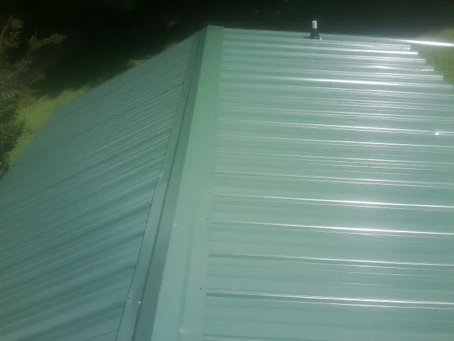 New green metal panels meeting at the ridge of a roof — Flat Roof Repair work by our crew in Wooster