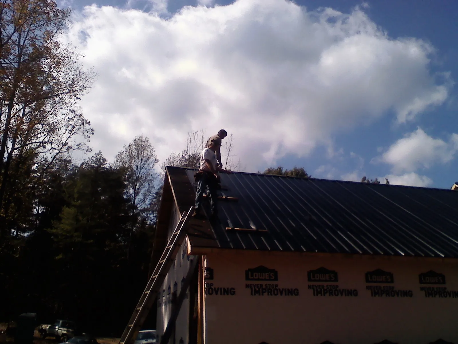 Roofer fastening dark metal panels high against a cloudy sky, from a Roof Inspection job in Wooster