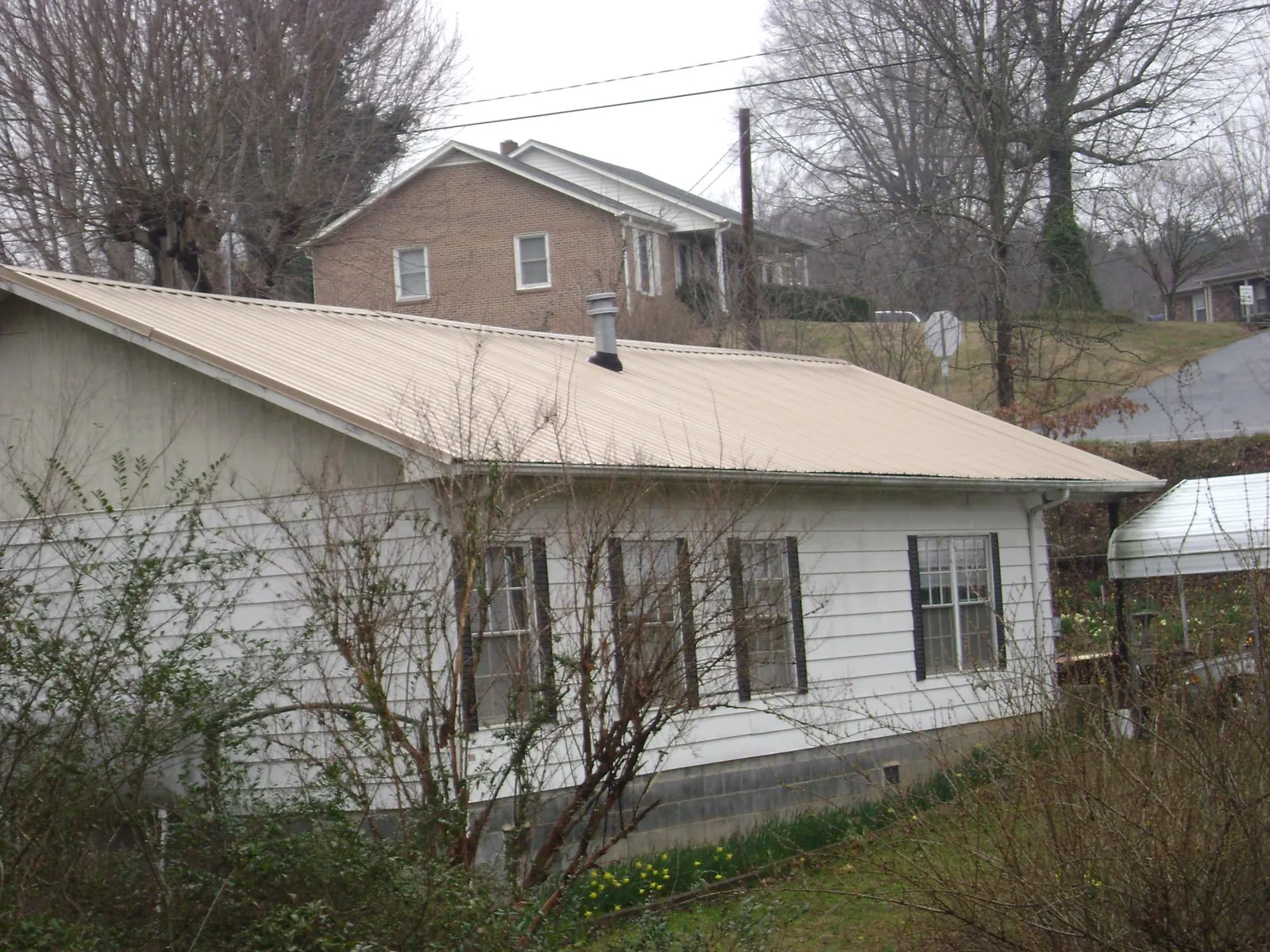 Tan metal roof on a white sided house set into a hillside — Commercial Roofing by Roofing Brothers in Wooster